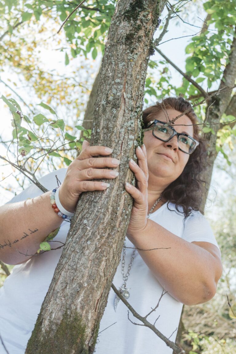 Elisabeth Schäffer steht lächelnd an einen Baum gelehnt – Symbol für Halt, Stärke und Verbundenheit