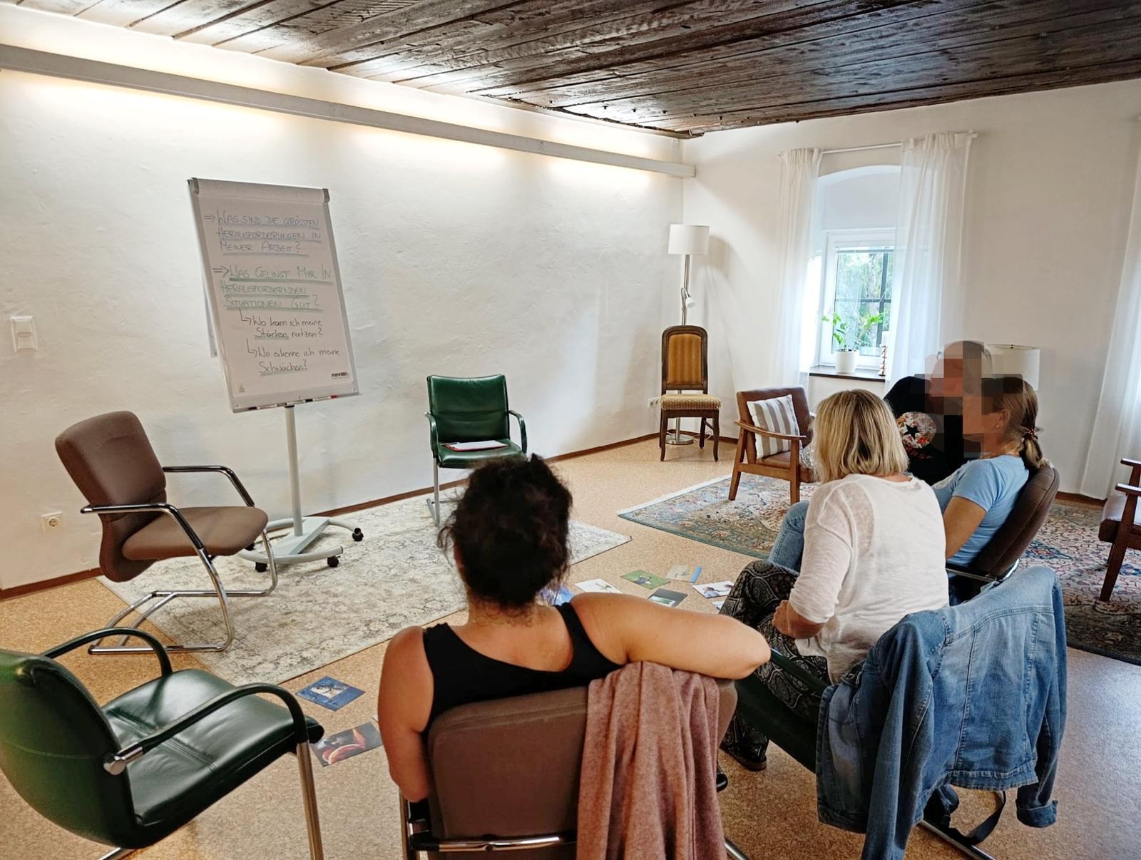 Vier Personen sitzen in einem Beratungsraum und blicken aufmerksam auf ein Flipchart – Gruppenarbeit bei Stephanie Illich.